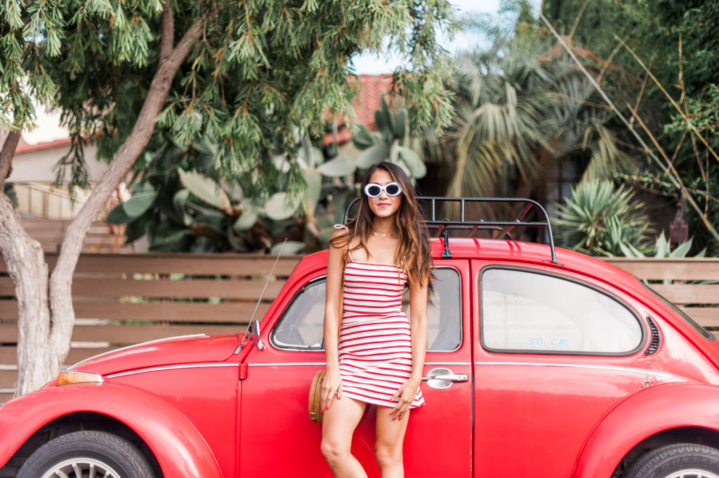 woman wearing striped white and red dress from reformation and leaning on a red car
